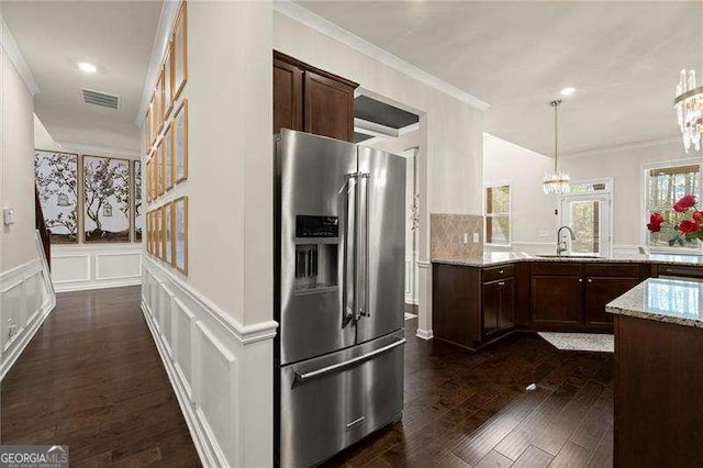 kitchen featuring a notable chandelier, light stone counters, high end refrigerator, a decorative wall, and a sink