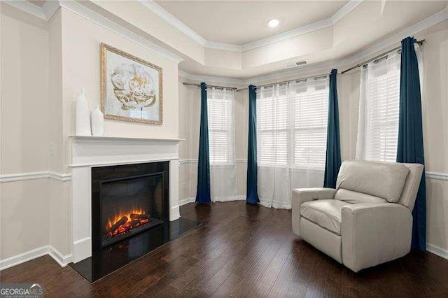 living area featuring baseboards, a raised ceiling, crown molding, wood finished floors, and a glass covered fireplace