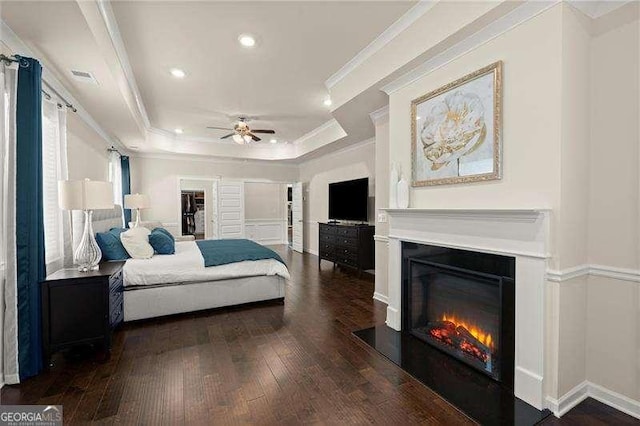 bedroom with a raised ceiling, ornamental molding, recessed lighting, hardwood / wood-style floors, and a glass covered fireplace