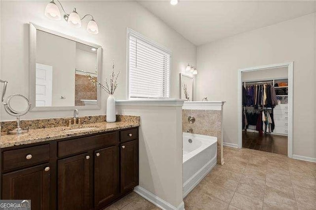 full bathroom featuring baseboards, a spacious closet, vanity, tile patterned flooring, and a garden tub