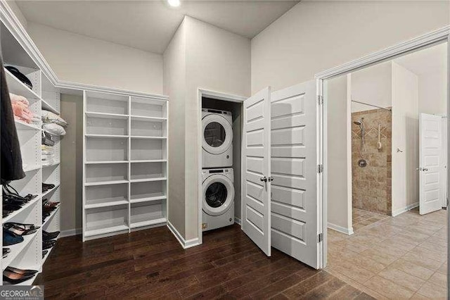 washroom with baseboards, stacked washer and dryer, laundry area, and wood finished floors