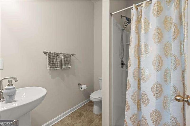 bathroom featuring curtained shower, baseboards, a sink, and toilet
