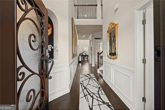 foyer entrance featuring arched walkways, a decorative wall, dark wood-type flooring, and wainscoting