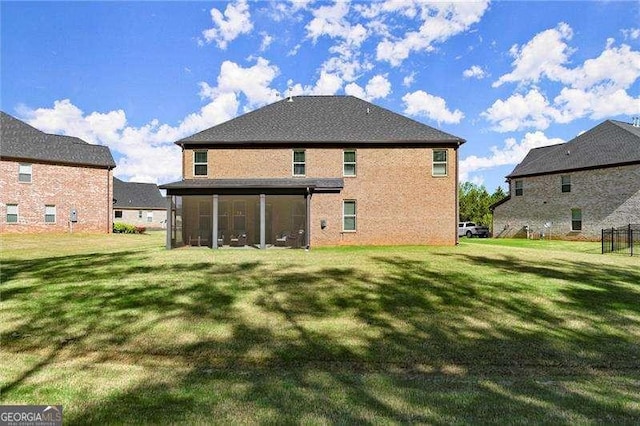 rear view of property featuring a sunroom, a yard, and brick siding