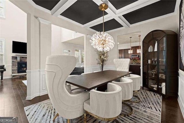 dining space with a decorative wall, a fireplace, beam ceiling, wood finished floors, and coffered ceiling