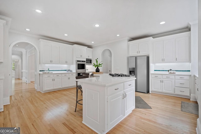 kitchen featuring white cabinets, arched walkways, ornamental molding, appliances with stainless steel finishes, and a kitchen bar