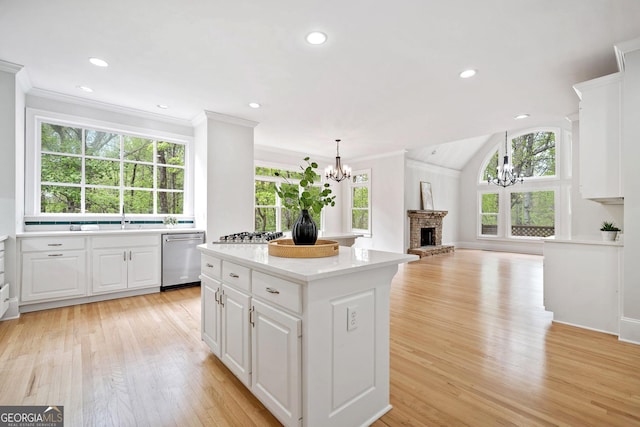 kitchen with a brick fireplace, a chandelier, crown molding, light wood finished floors, and stainless steel appliances