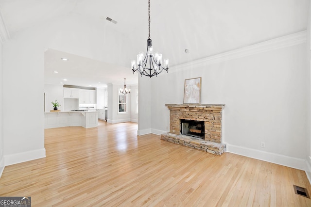 unfurnished living room with light wood finished floors, a notable chandelier, a stone fireplace, and visible vents