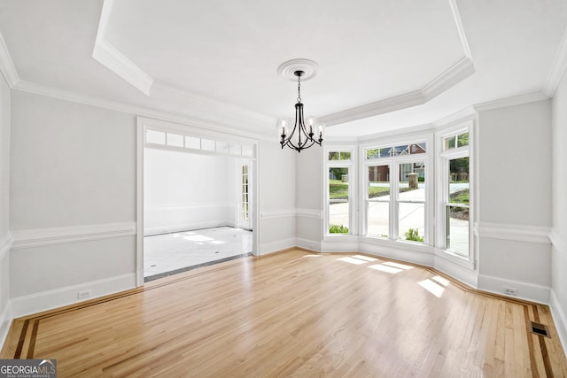 unfurnished dining area featuring a raised ceiling, wood finished floors, an inviting chandelier, and ornamental molding