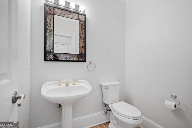 half bathroom with toilet, wood finished floors, and baseboards