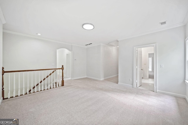 spare room featuring crown molding, baseboards, arched walkways, and light carpet