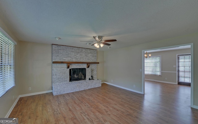 186 Foxdale Dr, Toccoa, GA 30577 - unfurnished living room with a textured ceiling, a brick fireplace, wood finished floors, baseboards, and ceiling fan with notable chandelier