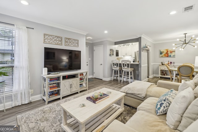 living room featuring ornamental molding, visible vents, a notable chandelier, and wood finished floors