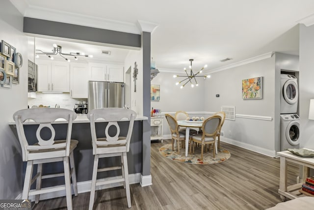 kitchen featuring an inviting chandelier, freestanding refrigerator, stacked washer / dryer, crown molding, and white cabinetry