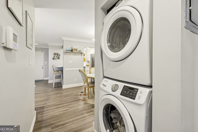 laundry area with baseboards, ornamental molding, stacked washer / dryer, laundry area, and wood finished floors