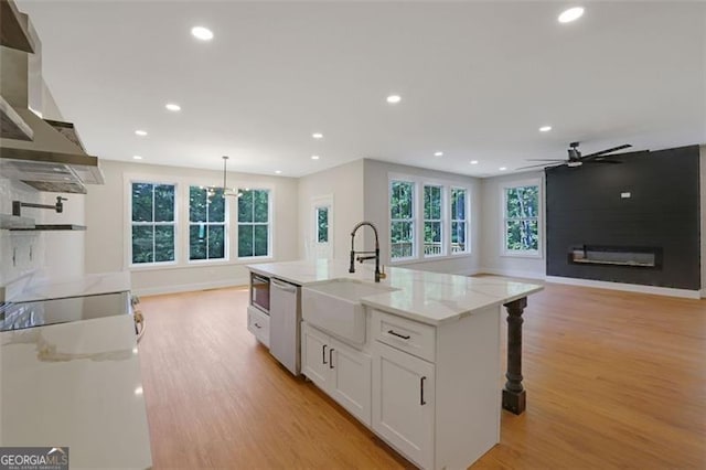 kitchen featuring dishwasher, a sink, wall chimney range hood, light wood-type flooring, and white cabinetry