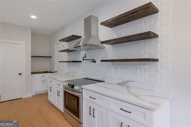 kitchen featuring stainless steel electric range oven, white cabinets, open shelves, wall chimney range hood, and light wood-type flooring