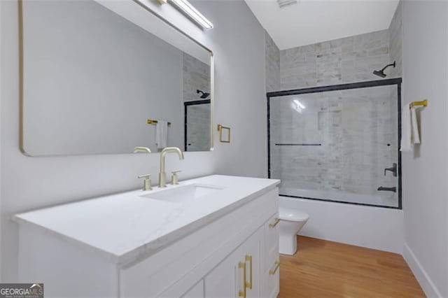 bathroom with combined bath / shower with glass door, vanity, toilet, and wood finished floors
