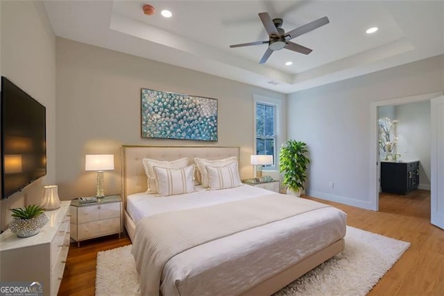 bedroom with a tray ceiling, baseboards, recessed lighting, and wood finished floors