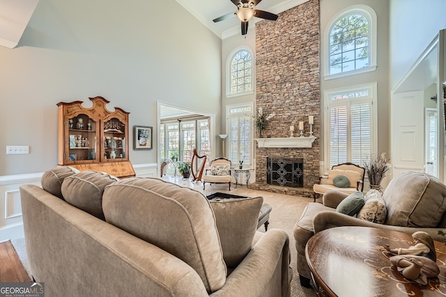living room with wainscoting, a healthy amount of sunlight, a ceiling fan, and a stone fireplace