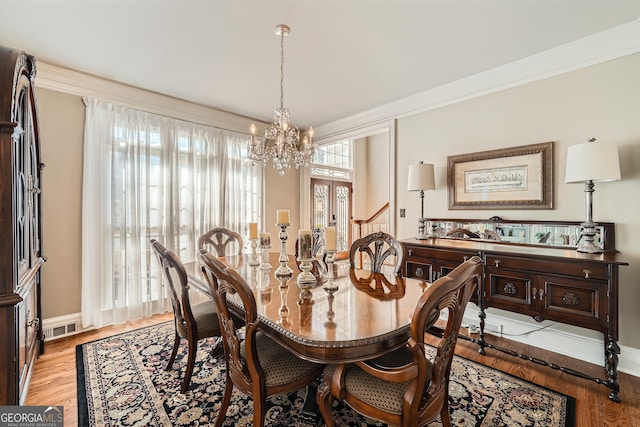 dining room featuring crown molding, visible vents, a chandelier, light wood finished floors, and baseboards