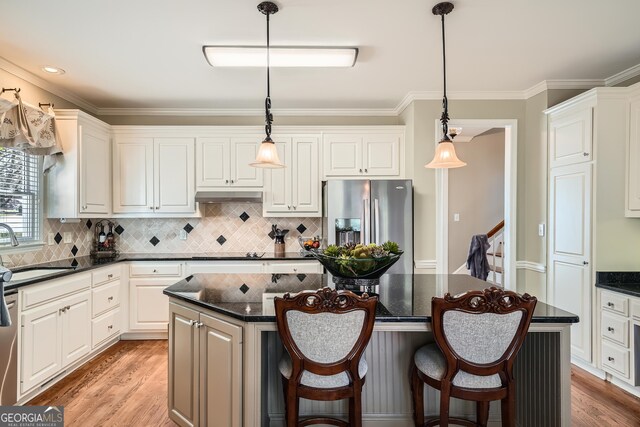 kitchen with a center island, a sink, appliances with stainless steel finishes, under cabinet range hood, and light wood-style flooring