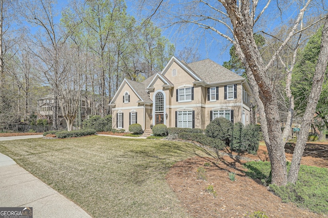 view of front of house with a shingled roof, stucco siding, and a front lawn
