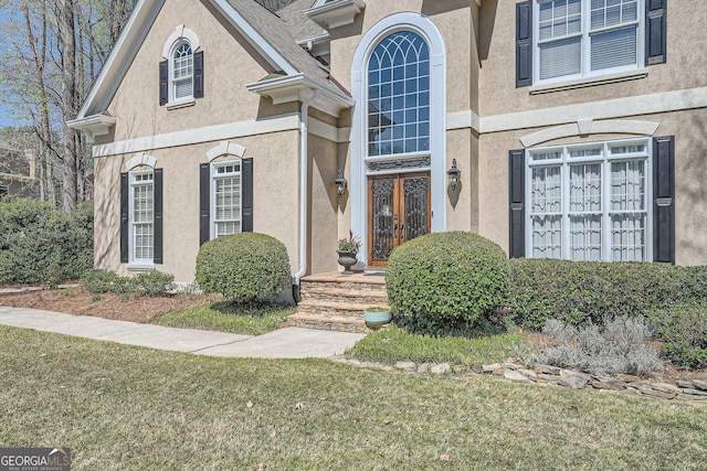 doorway to property featuring a lawn, french doors, and stucco siding