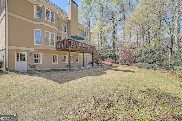 rear view of property featuring a patio area, a lawn, a chimney, stucco siding, and a wooden deck