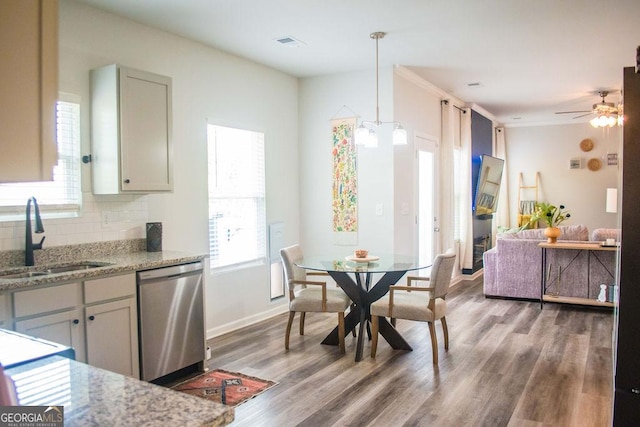 kitchen with stainless steel dishwasher, a sink, visible vents, decorative backsplash, and wood finished floors