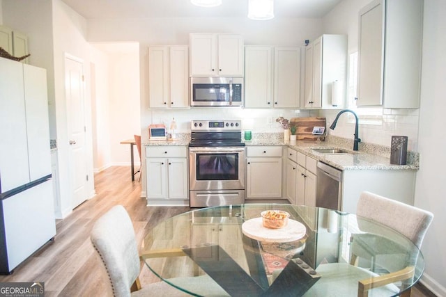 kitchen featuring tasteful backsplash, a sink, light wood-style floors, appliances with stainless steel finishes, and light stone countertops