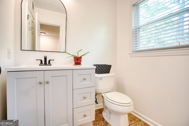 bathroom with baseboards, a healthy amount of sunlight, toilet, and vanity