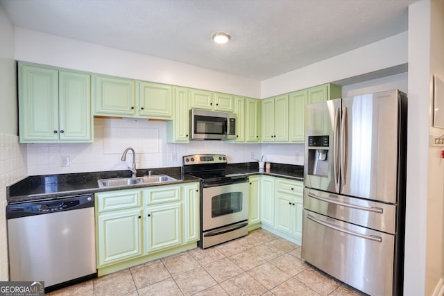 kitchen featuring light tile patterned floors, a sink, appliances with stainless steel finishes, backsplash, and green cabinets