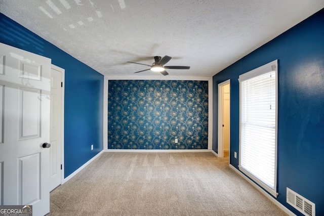 unfurnished room featuring a wealth of natural light, ceiling fan, carpet, and visible vents
