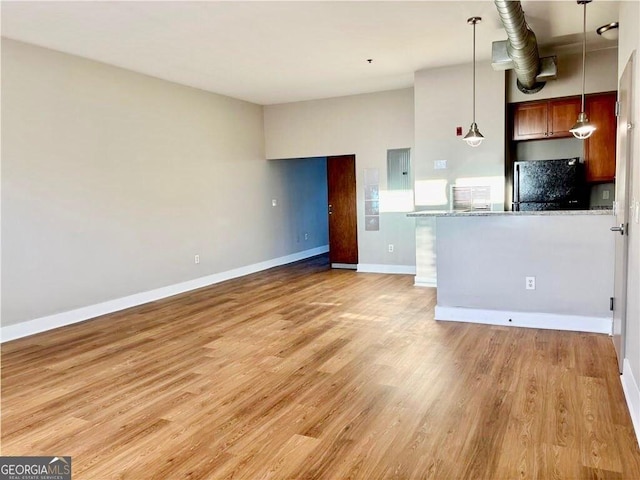 kitchen featuring baseboards, electric panel, light wood-style flooring, freestanding refrigerator, and hanging light fixtures