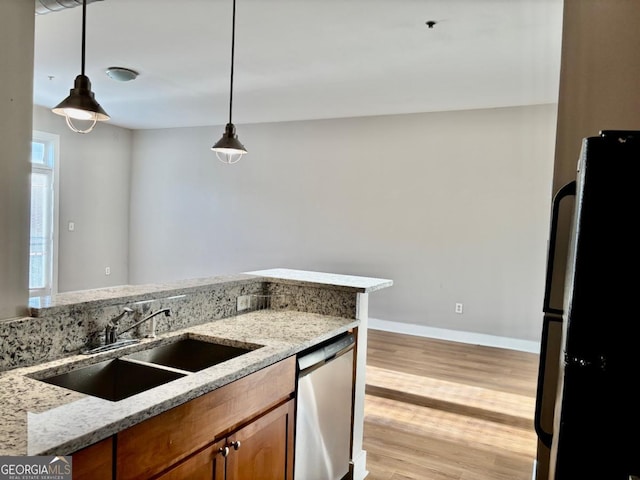 kitchen featuring stainless steel dishwasher, freestanding refrigerator, a sink, brown cabinets, and light wood finished floors