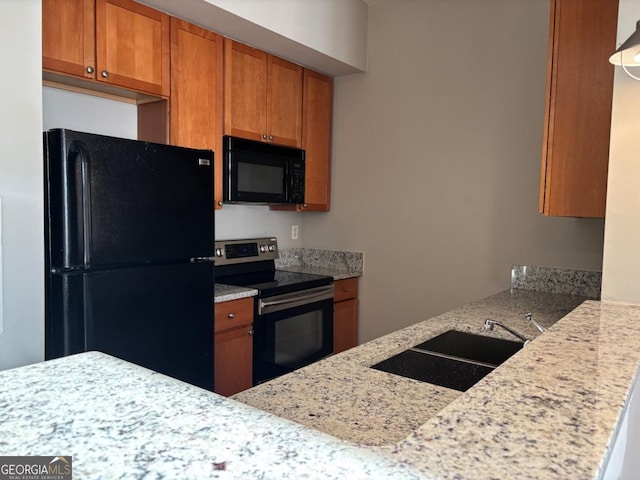 kitchen with brown cabinetry, a sink, black appliances, and light stone counters