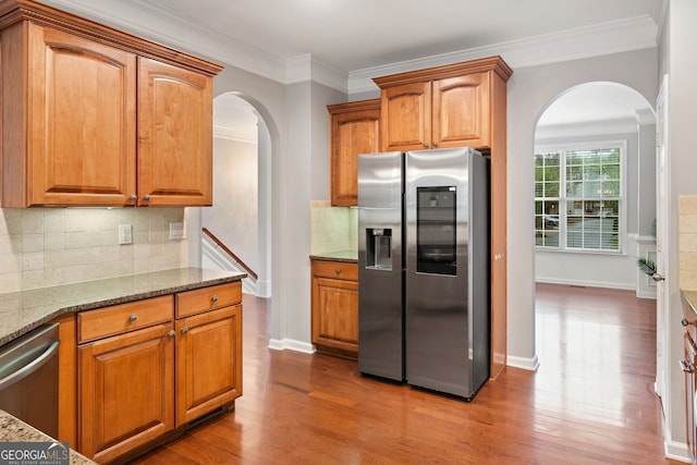 kitchen featuring crown molding, arched walkways, stone counters, wood finished floors, and stainless steel appliances