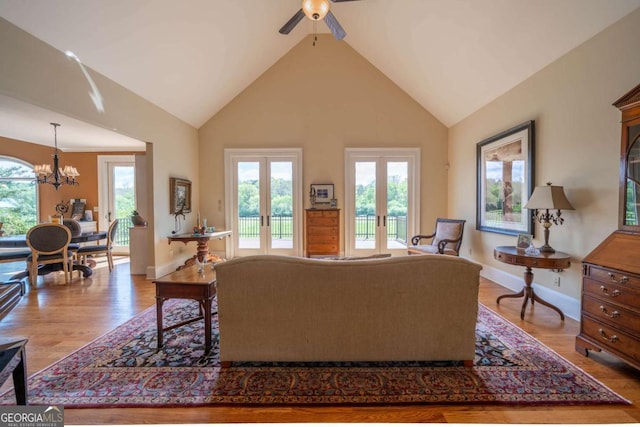 living room featuring baseboards, wood finished floors, ceiling fan with notable chandelier, french doors, and high vaulted ceiling