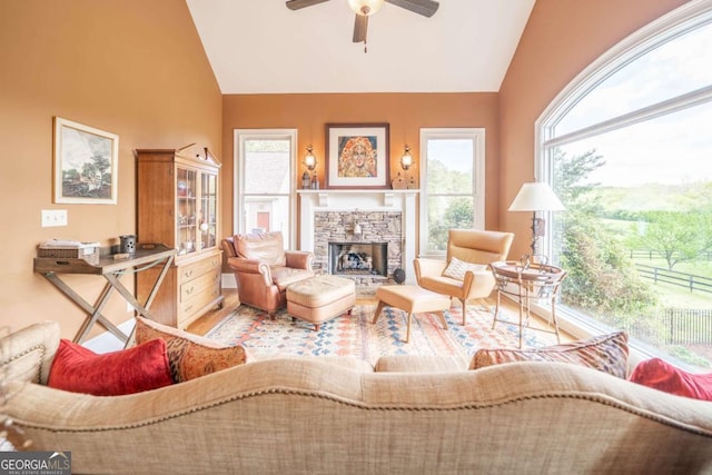 living room featuring wood finished floors, ceiling fan, a stone fireplace, and vaulted ceiling