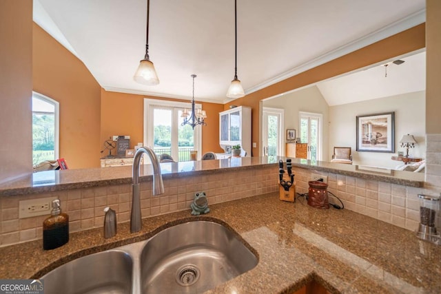 kitchen with crown molding, vaulted ceiling, dark stone countertops, a sink, and hanging light fixtures