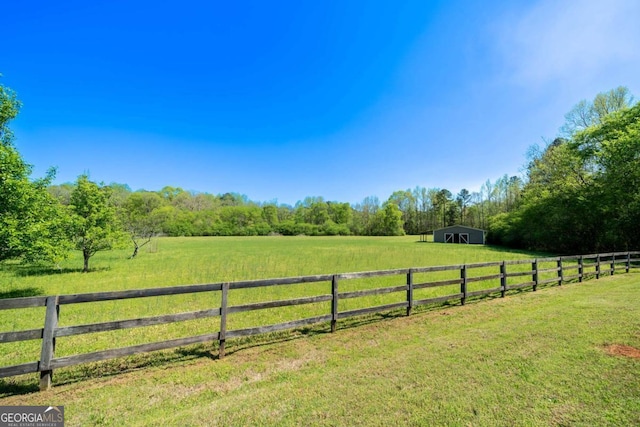 view of yard featuring a rural view, a view of trees, fence, and an outbuilding