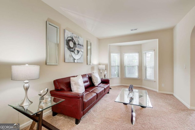 carpeted living area featuring visible vents, baseboards, and arched walkways