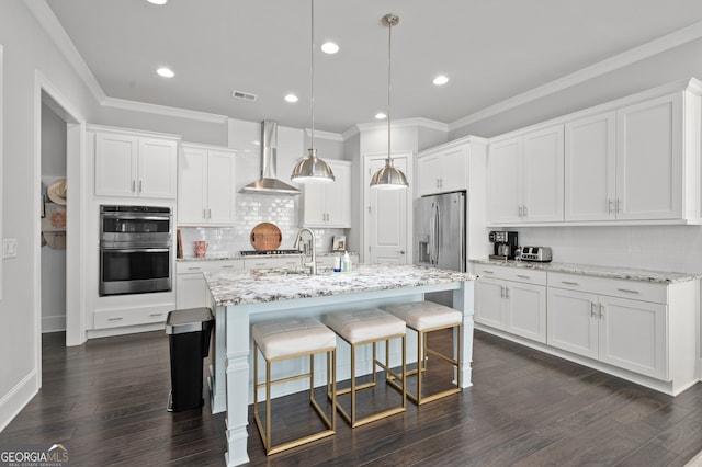kitchen featuring visible vents, wall chimney exhaust hood, appliances with stainless steel finishes, a kitchen breakfast bar, and white cabinetry