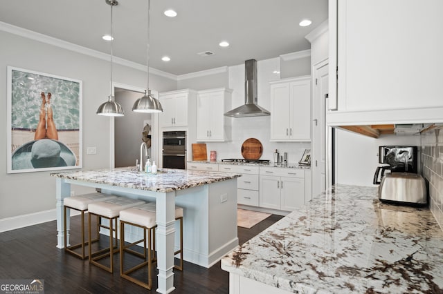 kitchen featuring tasteful backsplash, wall chimney exhaust hood, ornamental molding, appliances with stainless steel finishes, and an island with sink