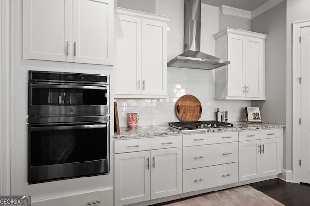 kitchen featuring wall chimney range hood, stainless steel appliances, white cabinetry, and decorative backsplash