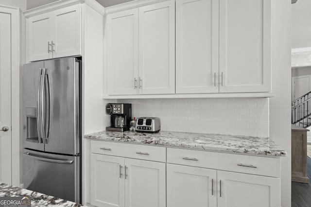 kitchen featuring stainless steel refrigerator with ice dispenser, light stone countertops, white cabinetry, and backsplash