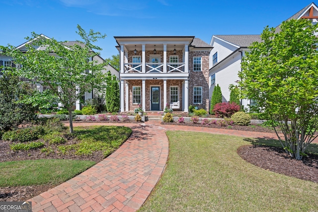view of front facade with brick siding, covered porch, a front yard, and a balcony