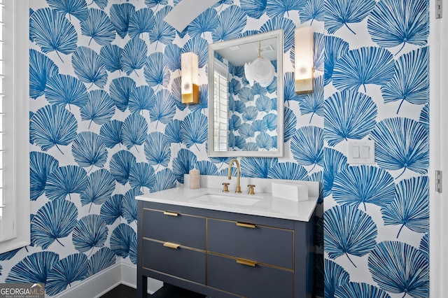 half bath featuring baseboards, vanity, and wallpapered walls
