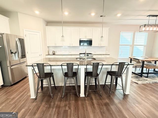 3495 Delegate Aly, Scottdale, GA 30079 - kitchen with decorative backsplash, stainless steel appliances, a center island with sink, white cabinetry, and dark wood-style floors